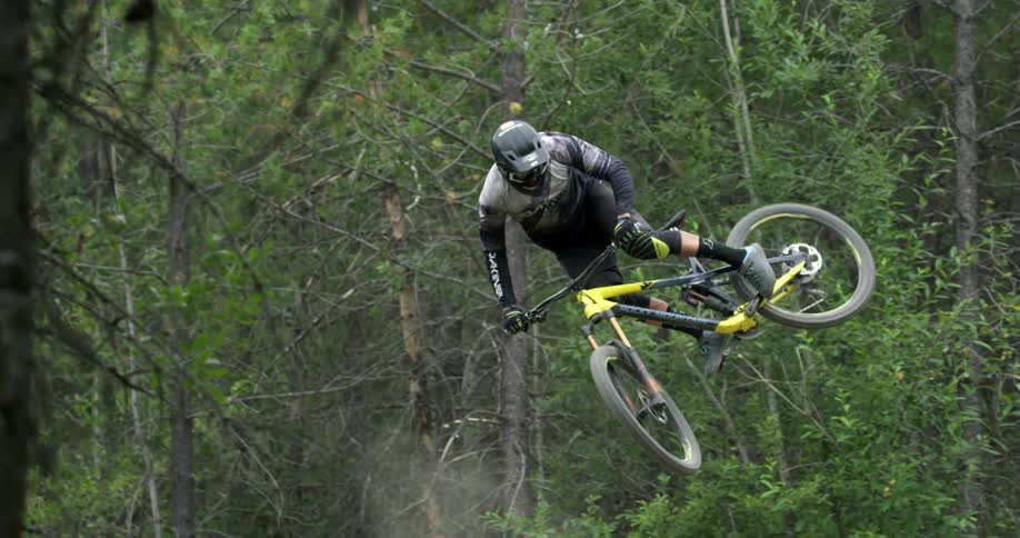 A mountain biker whips his bike sideways on a forest jump 2