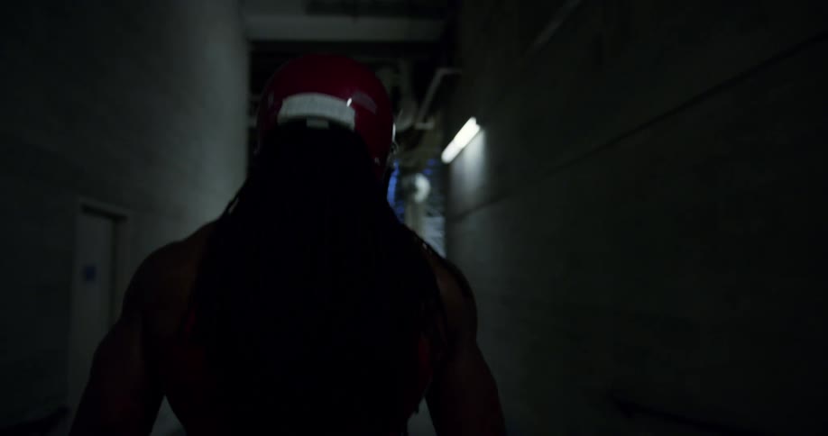A man wearing a red helmet walks down a dimly lit hallway that leads to an underground parking garage
