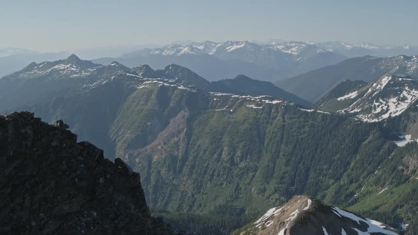A large mountain range with a forest growing up the slope and a dusting of snow visible