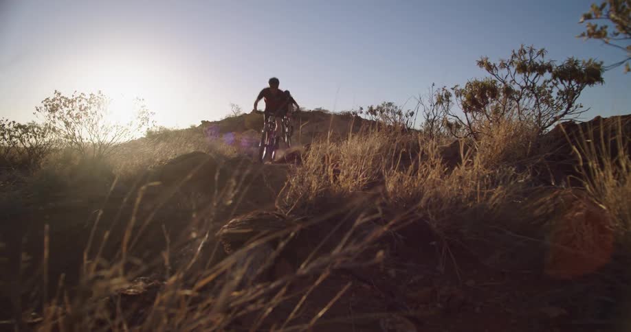 A pair of cyclists hitting a small jump while riding trails on their mountain bikes