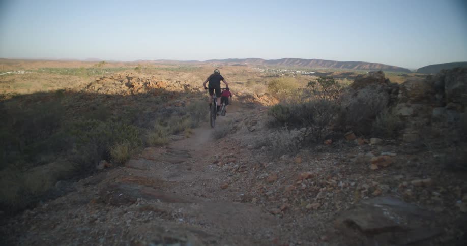 Two mountain bike riders jump over a gap on a mountain trail