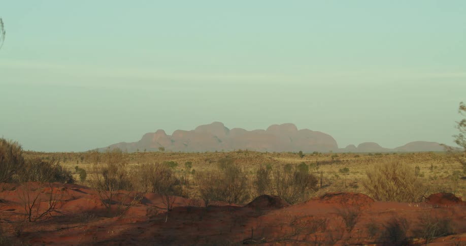 Grass stretches across outback with Khata Tjuta mountains in distance