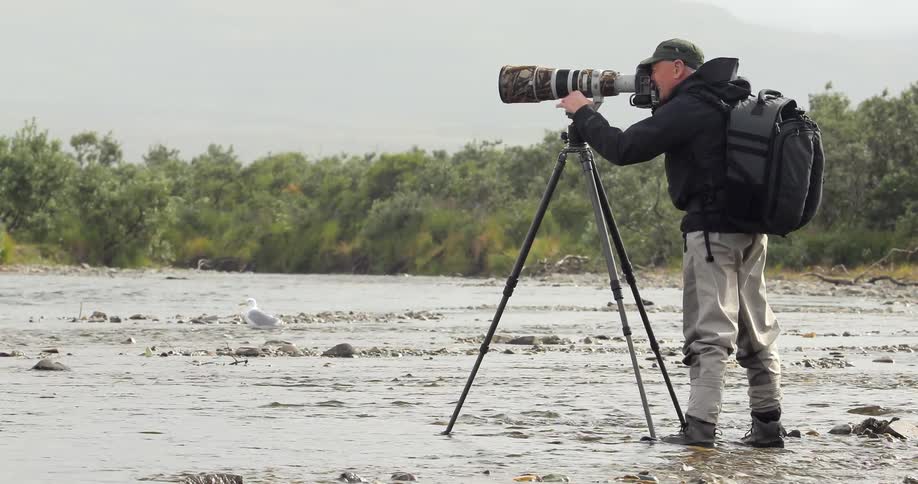 A photographer takes a picture while standing in moving water