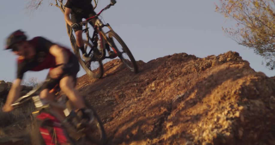 Two bicyclists ride down slanted rock wall ride