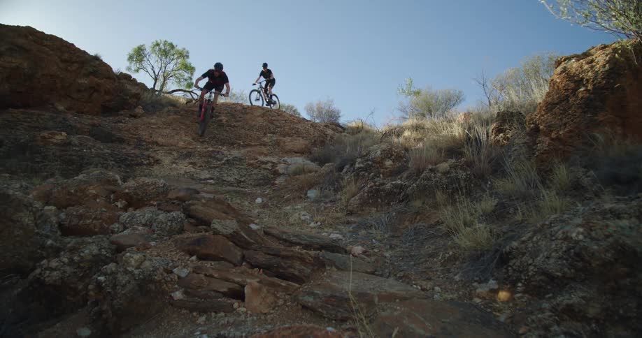 Two people mountain bike down a rocky hill