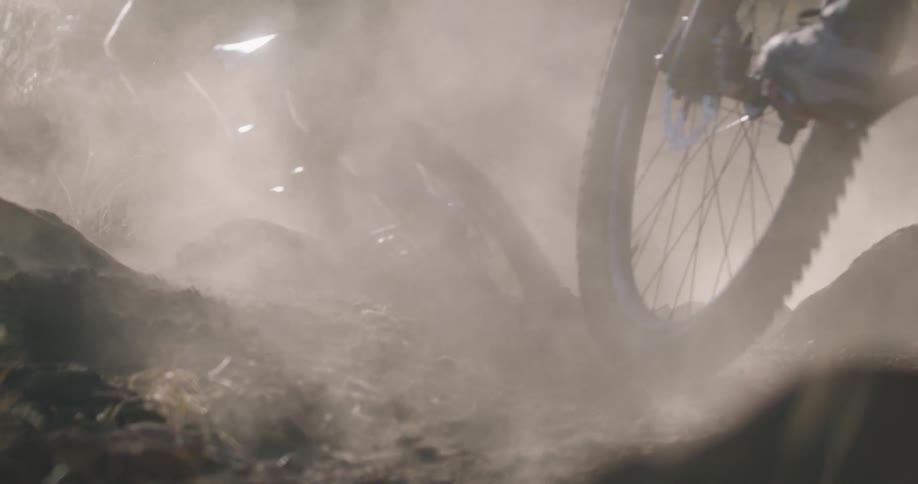 A pair of cyclists making a sharp turn on a dirt path causing dust to kicked up