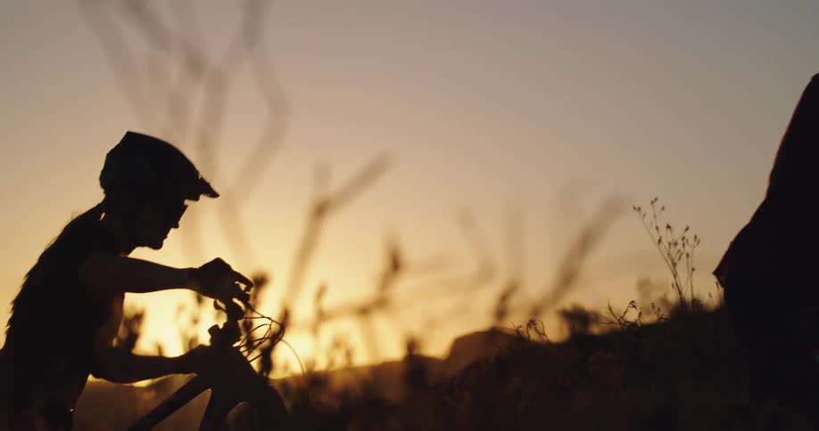 A man and woman push their bikes through a hillside at sunset