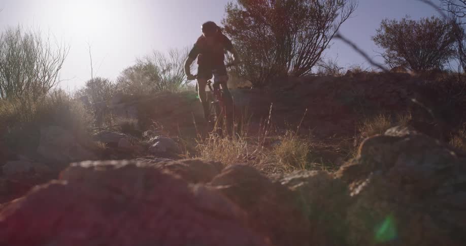 Two mountain bikers jump their bikes on a rugged dirt trail out in the desert