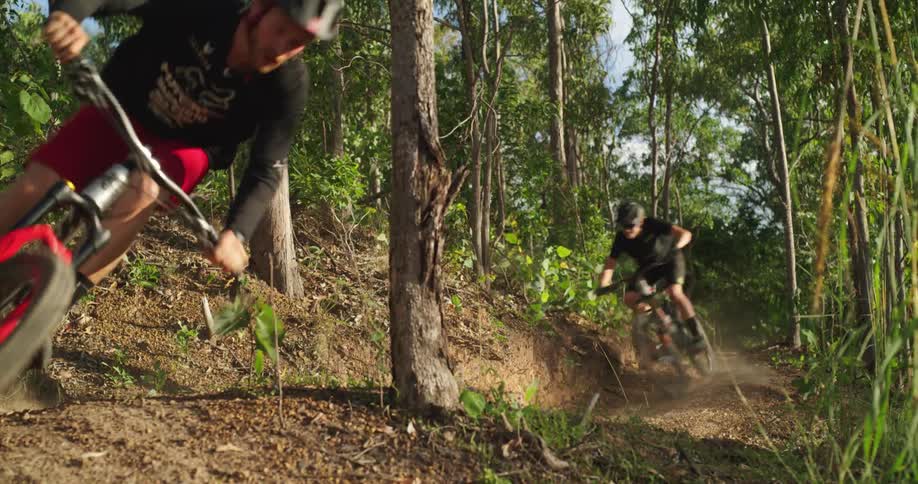 Two bicyclists ride on a dirt trail in a forested area