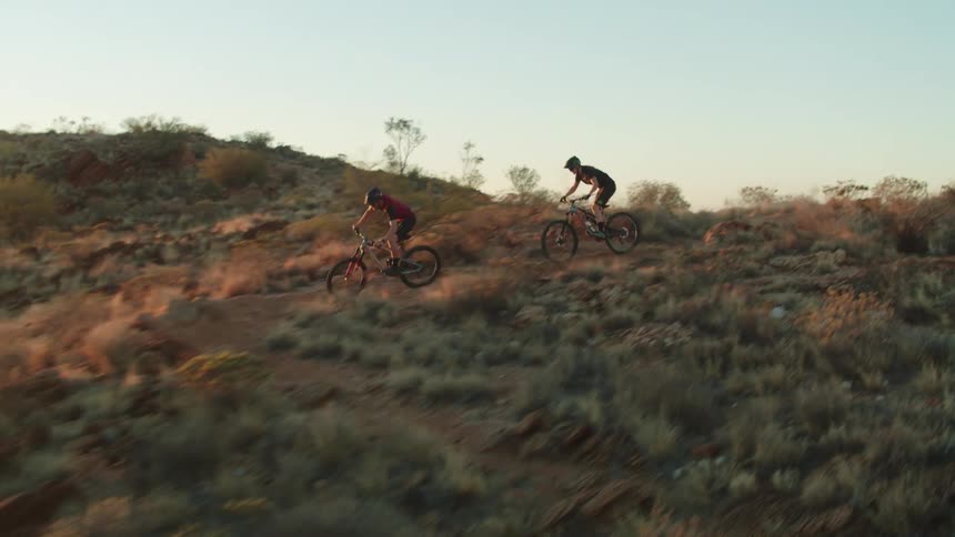 Two bicyclists ride over rough desert terrain on mountain bikes