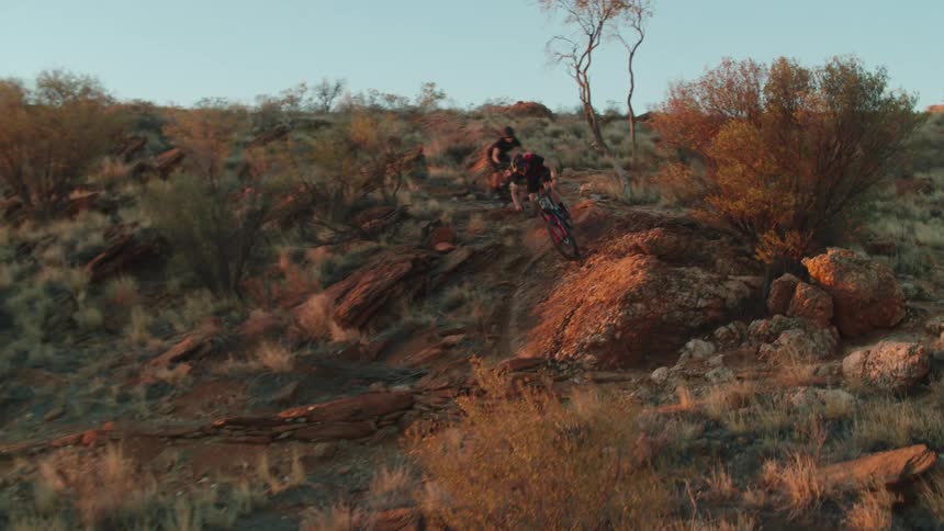 Two mountain bikers ride down a rocky trail covered with desert brush