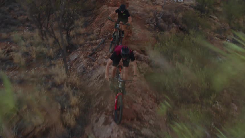Man and woman mountain bike down rugged dirt trail on desert mountain