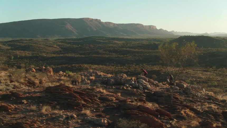 A pair of mountain cyclists pedaling up a rocky hill in a vast countryside