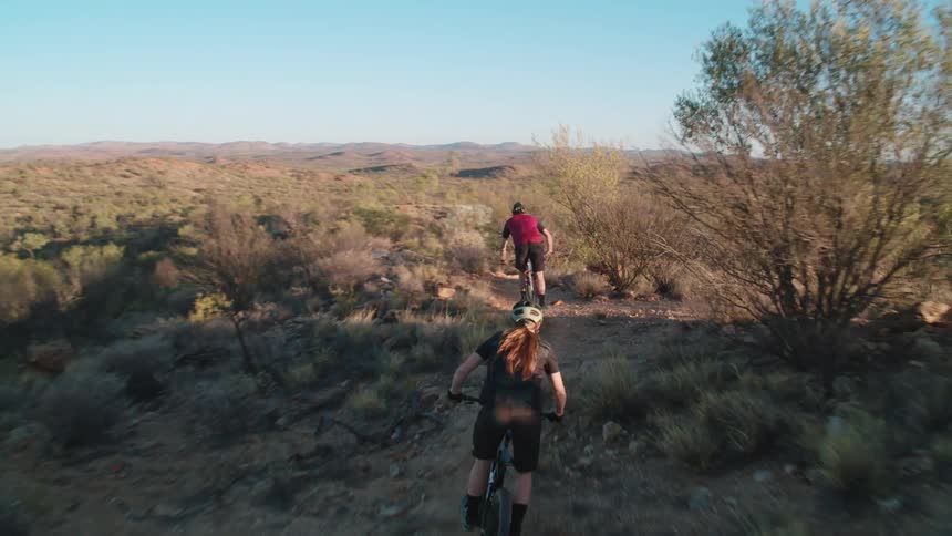 Two people ride bikes over a dirt trail in a desert