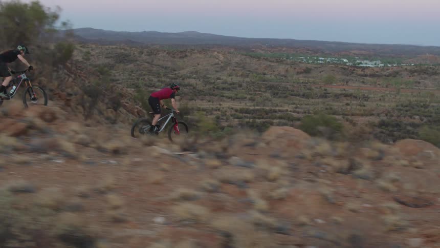 Two people mountain bike down the rocky terrain at dusk