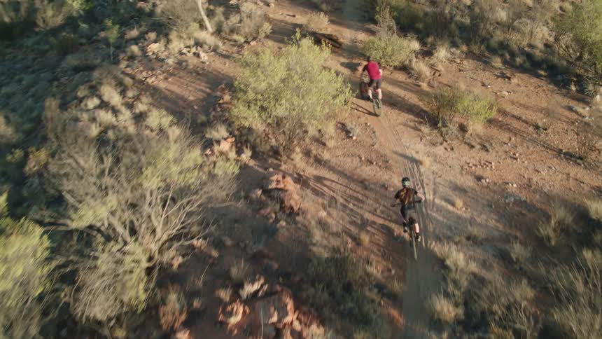 Two people mountain bike over rough terrain