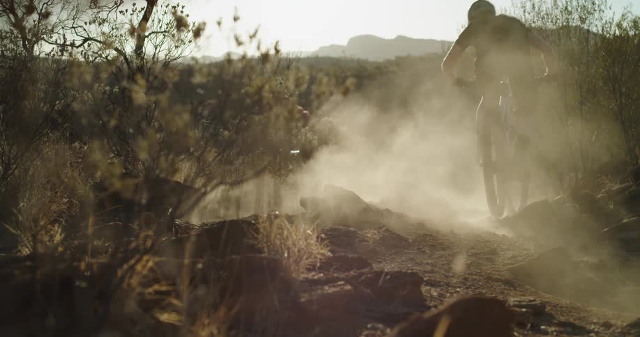 Two people mountain bike around dirt corner kicking up dust