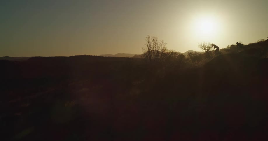 Two mountain bikers ride down a hill at sunset