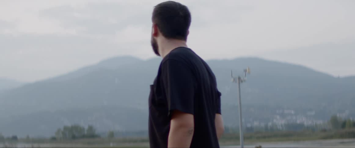 A man in a black t shirt and a moustache walks around outside checking out the scene searching for something