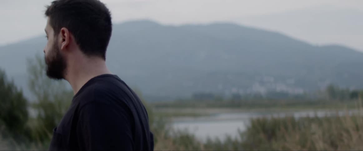 Man walking near river and grassland looks over shoulders behind him
