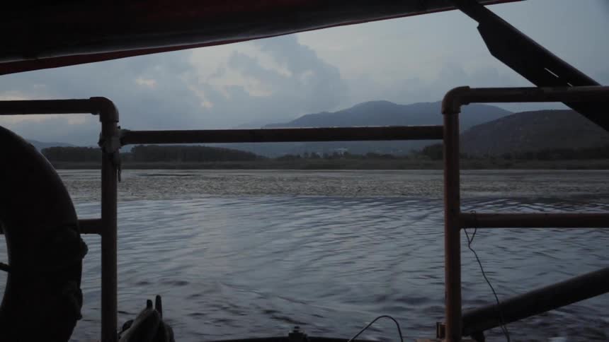 A boat sails up a river off the coast of a mountain range