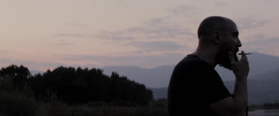 A man standing smoking a cigarette with the mountains in the background