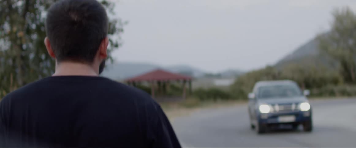 A man walking along the side of a road as a vehicle drives pass in the opposite direction