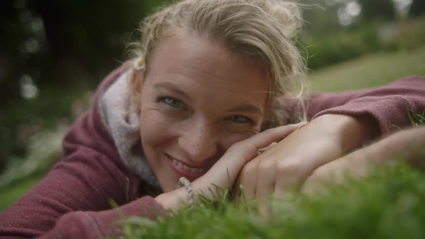 A woman is holding a mans hand as she lays on some grass