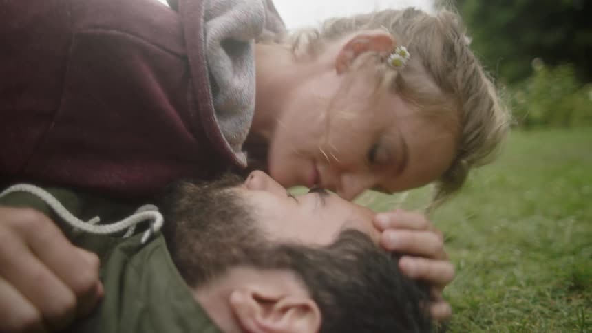 A couple lie on the grass outdoors and cuddle together