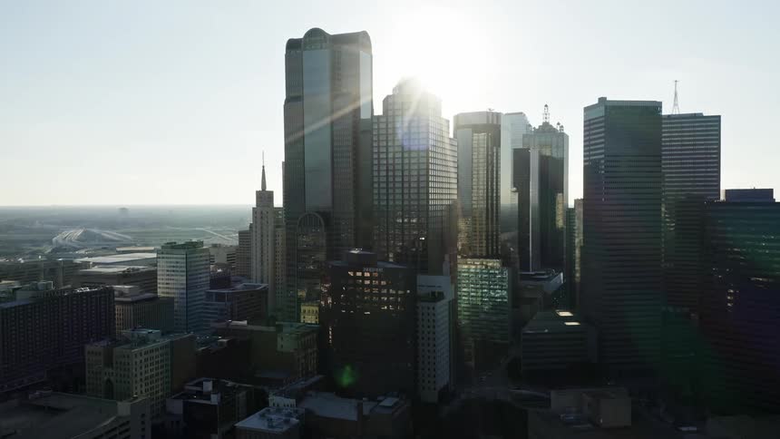 The sun shines through a dense urban skyline filled with skyscrapers