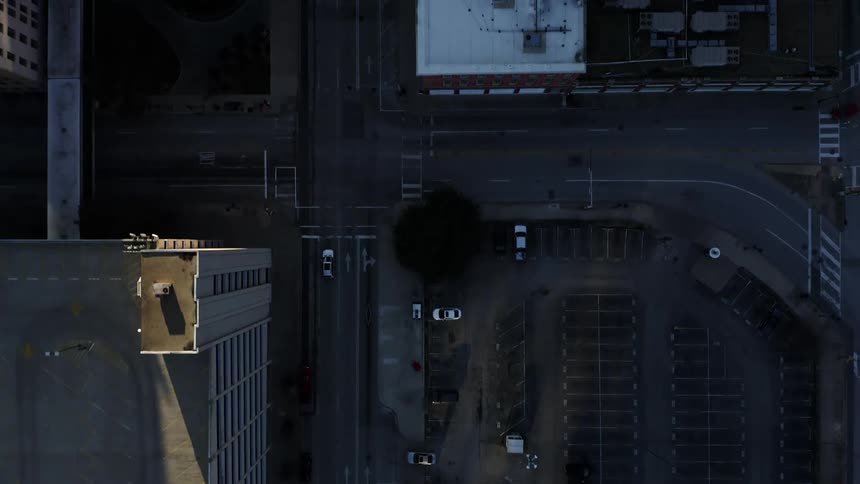 Cars travel past city buildings and almost empty parking lots