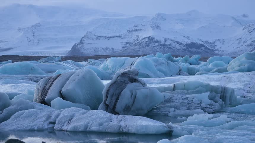 Large chunks of ice float on some water near mountains