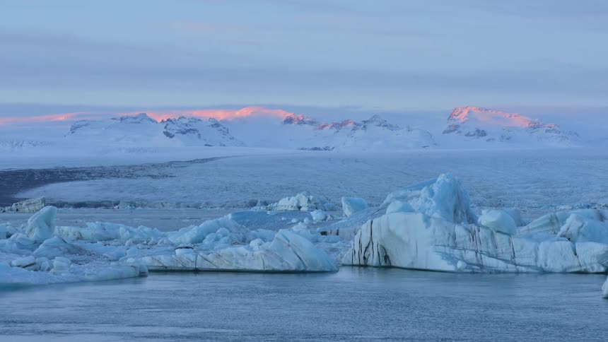 Icebergs float in an ocean as snow covered mountains loom in the distance