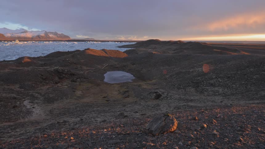 Sunrise on gray rocky shore with frozen icy water