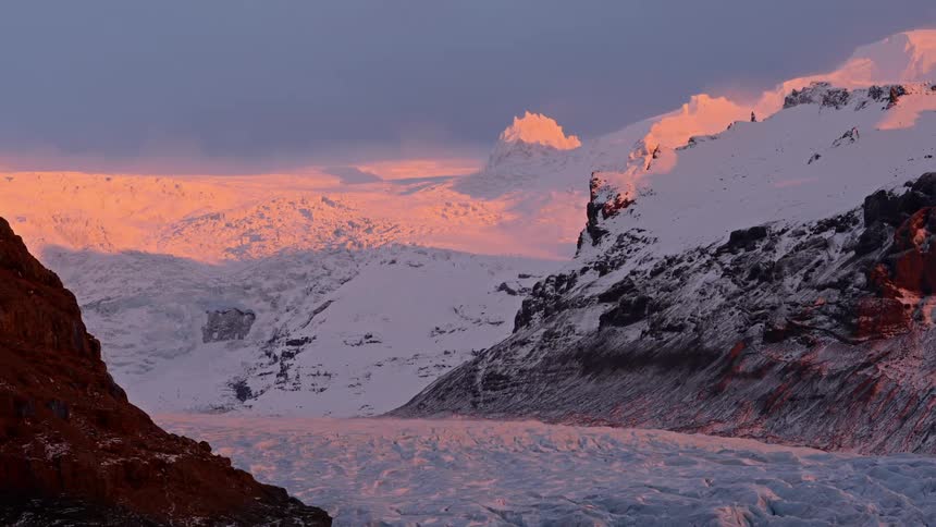 Sunlight glows peach on the snow covered ridge