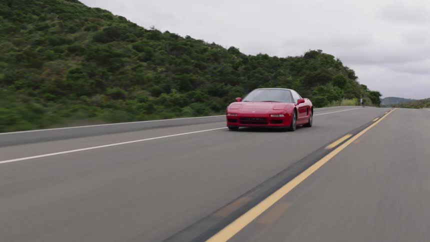 Acura NSX sports car speeding down a road through a hilly countryside