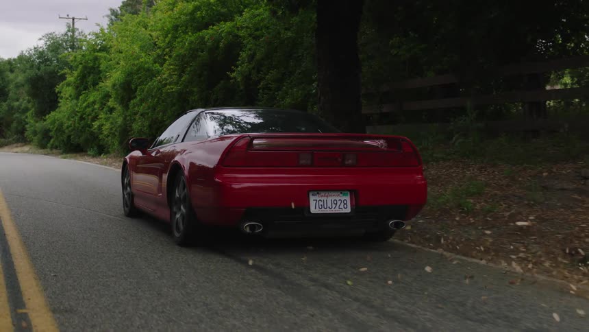 A red sports car traveling down a road through a woodland as fallen leaves scatter and whirl in its wake