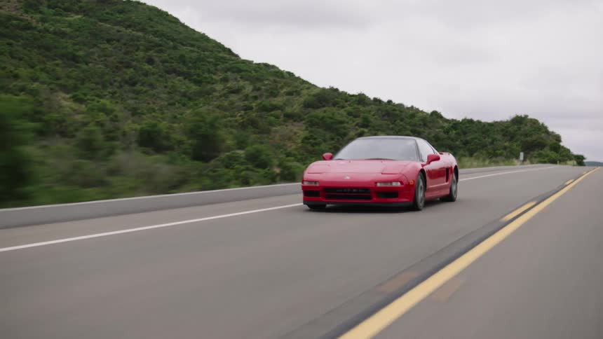 A red sports car drives down a highway through a mountain valley