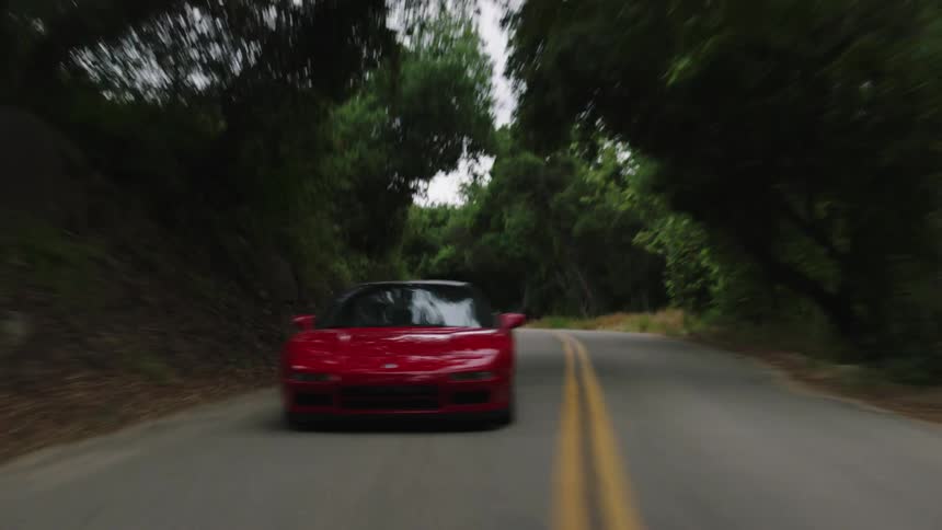 A red sports car drives down a road in a forest
