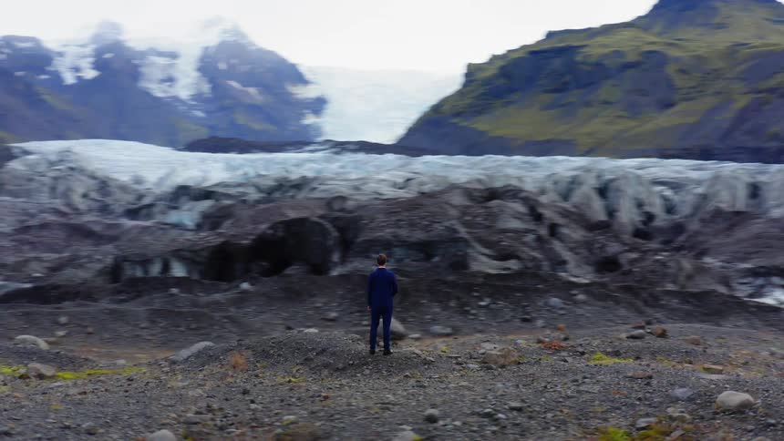 A man in a blue suit stands among a mountain range