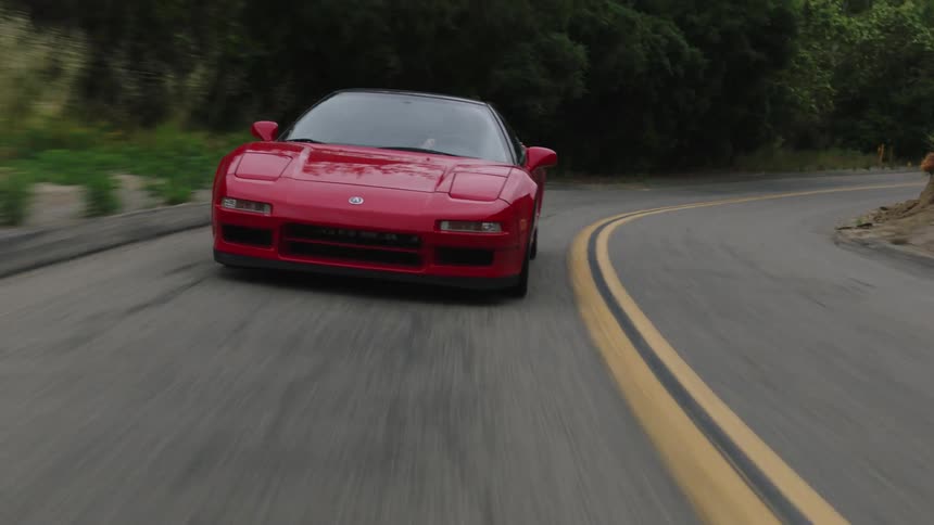 Red sports car drives along curving highway through forest near mountain slope