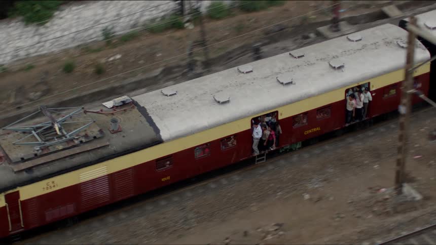 Passengers crowd into the doorways of a train as it makes it way down the track in a developing country