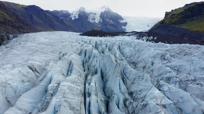 A glacier of ice and snow sits in a valley between two mountains