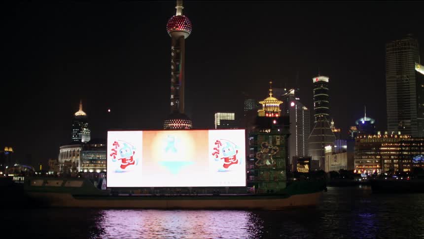 Digital display on large ship passes brightly lit city downtown at night