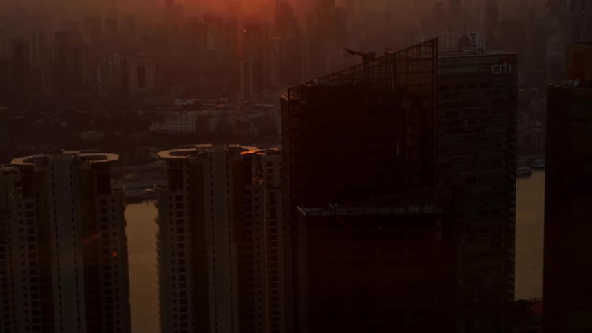 The sun hangs low in the sky over a dense downtown urban area