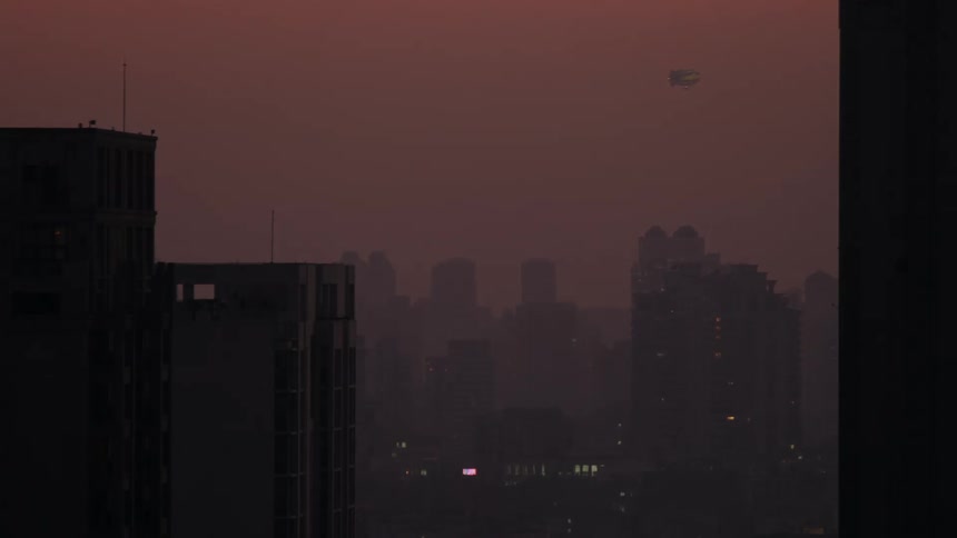 A blimp flies over skyscrapers in a hazy city at dusk