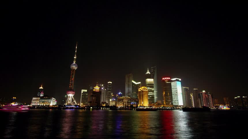 Boats float in front of city skyscrapers at night