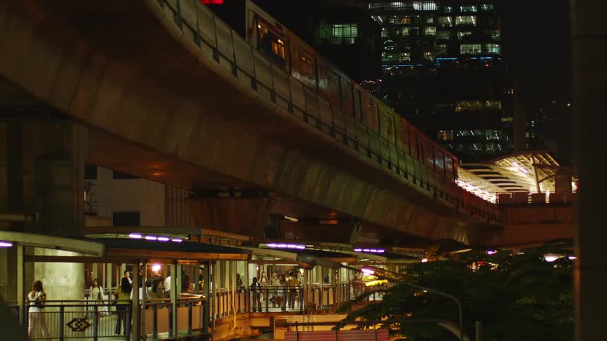 Crowds of people walk around a train station as a train leaves via a rail overhead
