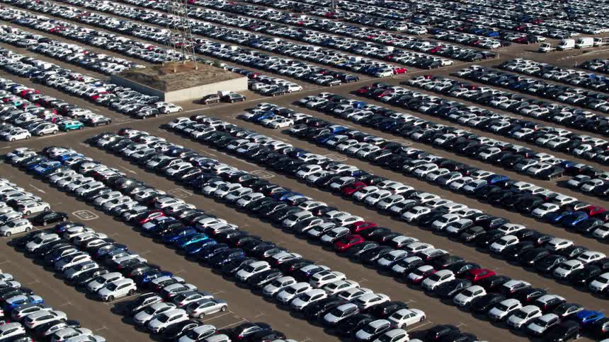 Numerous cars sit parked in a large lot with a building in the middle