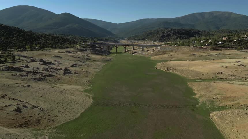 Riverbed with green vegetation runs under bridge in front of mountains